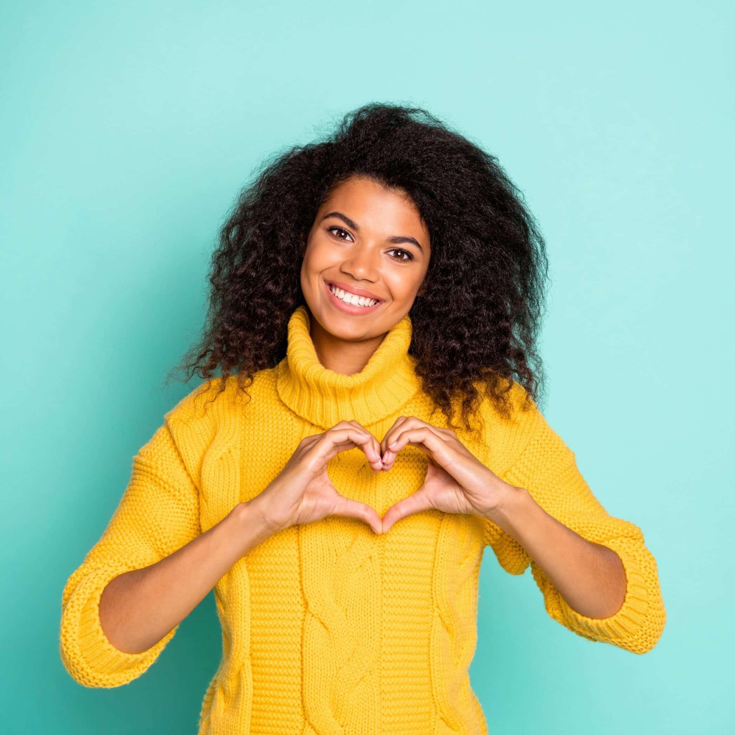Photo of amazing dark skin lady holding hands in heart figure symbolizing, cardiac health care wear yellow knitted pullover isolated blue teal color background
